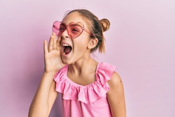 Beautiful brunette little girl wearing heart shaped sunglasses shouting and screaming loud to side...