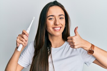 Young hispanic girl holding electric toothbrush smiling happy and positive, thumb up doing...