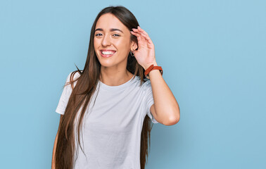 Young hispanic girl wearing casual white t shirt smiling with hand over ear listening an hearing to rumor or gossip. deafness concept.