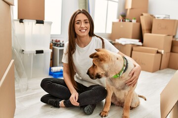 Young hispanic woman smiling confident hugging dog sitting on floor at new home