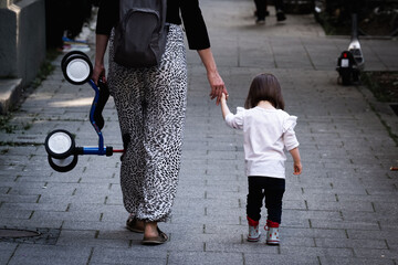 Woman walking down a paved sidewalk holding a child's hand and a tricycle