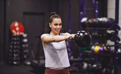 Smiling young woman swinging a dumbbell at the gym