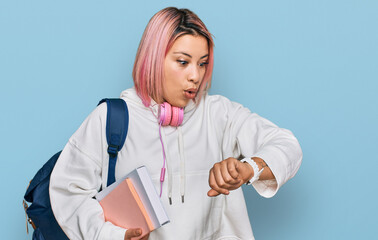 Hispanic woman with pink hair wearing student backpack and headphones looking at the watch time...