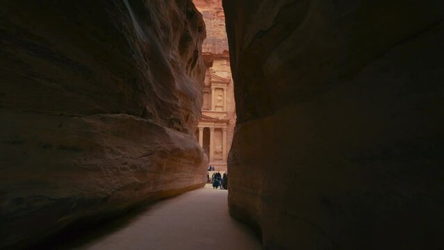 Walking toward The Treasury at Petra through the Siq, historic UNESCO heritage site carved into sandstone in Jordan. Famous Indiana Jones movie filming location and tourist destination Khaznet.