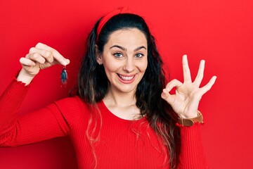 Young hispanic woman holding cockroach doing ok sign with fingers, smiling friendly gesturing excellent symbol - obrazy, fototapety, plakaty
