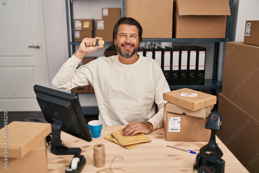 Canvas Prints Handsome middle age man working at small business ecommerce holding bitcoin looking positive and happy standing and smiling with a confident smile showing teeth