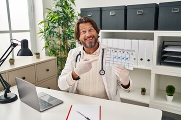 Handsome middle age doctor man holding holidays calendar smiling happy pointing with hand and finger
