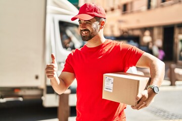 Young hispanic man courier holding package doing ok gesture at street