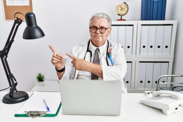 Senior caucasian man wearing doctor uniform and stethoscope at the clinic pointing aside worried...
