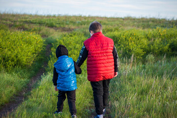 Naklejka na ściany i meble Children in the open spaces of the field are walking among the juicy spring grass in the light of sunset along a narrow trampled path