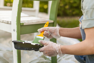 Painting Chair to green color with brush in protective gloves. Worker paints garden furniture green.