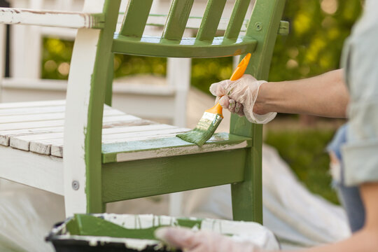 Painting Chair with brush in protective gloves. Worker paints garden furniture green. Renewing, Renovation Wooden Garden Furniture