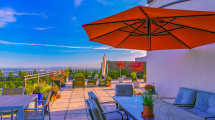 Red patio umbrella over glass patio table on rooftop patio garden with panoramic views during the...