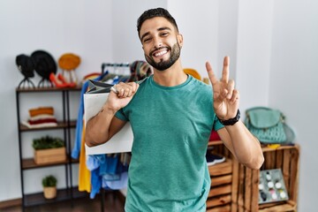 Young handsome man with beard holding shopping bags at retail shop smiling looking to the camera...