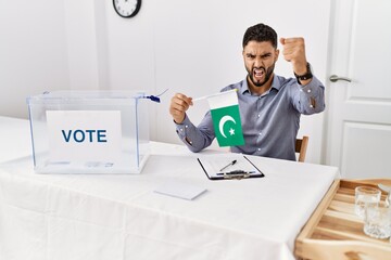 Young handsome man with beard at political campaign election holding pakistan flag annoyed and frustrated shouting with anger, yelling crazy with anger and hand raised - obrazy, fototapety, plakaty