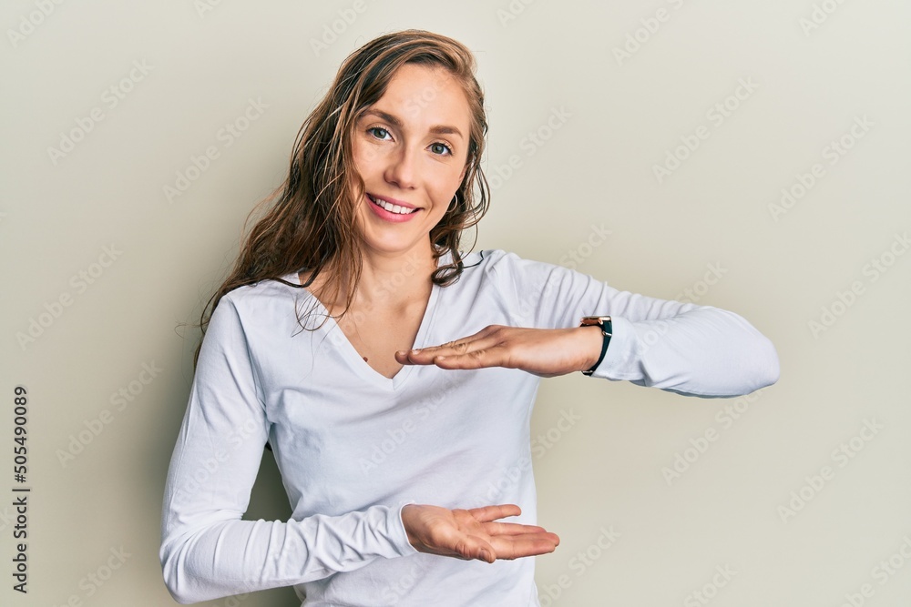 Canvas Prints Young blonde woman wearing casual clothes gesturing with hands showing big and large size sign, measure symbol. smiling looking at the camera. measuring concept.