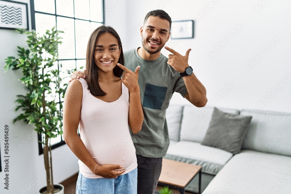 Poster young interracial couple expecting a baby, touching pregnant belly smiling cheerful showing and poin