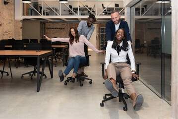 Four cheerful young multiracial entrepreneurs having fun while running around in office chairs and smiling