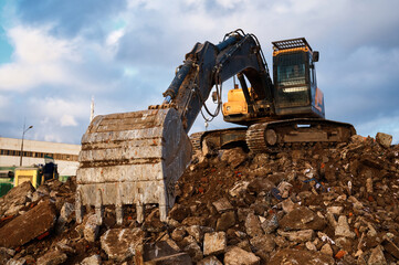 Bucket of excavator digs leftovers of destroyed building