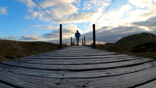 Young man passing by, static shot. Walking on wooden board walkaway in nature