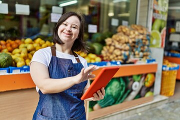 Young down syndrome woman wearing apron using touchpad at fruit store