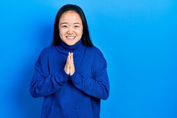 Young chinese girl wearing casual clothes praying with hands together asking for forgiveness smiling confident.