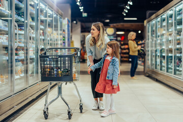 Young mom and her little daughter smiling and buying food - obrazy, fototapety, plakaty