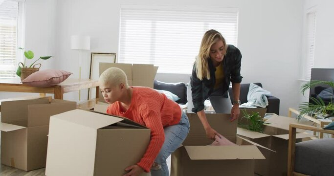 Happy diverse female couple talking and holding boxes during moving home