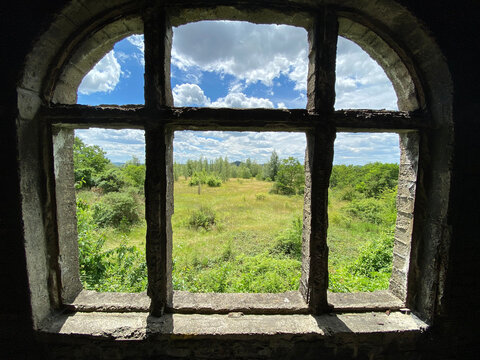 Closeup of an old window with stone rails against the green field and blue cloudy sky.