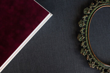 A velvet burgundy photo book endpaper with white pages and a copper vintage baroque frame lie on a dark gray fabric indoors.