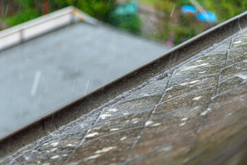 Heavy rain falling on the roof overflowing the gutter with water in rainy weather.
