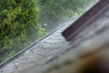 Heavy rain falling on the roof overflowing the gutter with water in rainy weather, visible roof...