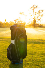 Fototapeta premium Sunlight streaming through golf clubs in bag on grassy landscape against clear sky at golf course