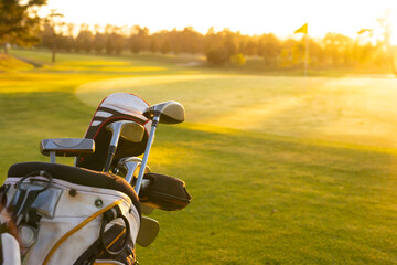 Fototapeta premium Golf clubs in bag on grassy landscape against clear sky at golf course during sunset, copy space