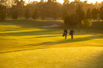 Multiracial young male friends with golf bags walking against trees at golf course during sunset