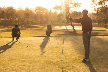 African american young man holding flag while playing golf with caucasian friend at golf course