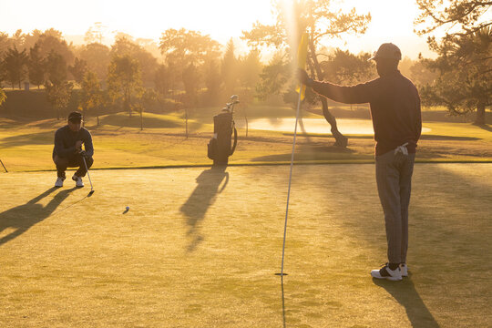 African american young man holding flag while playing golf with caucasian friend at golf course