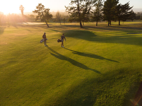 Aerial view of multiracial young male friends with bags walking on golf course during sunset