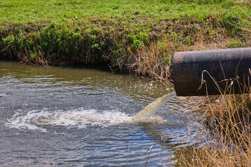 Draining sewage from pipe into river, pollution rivers and ecology.