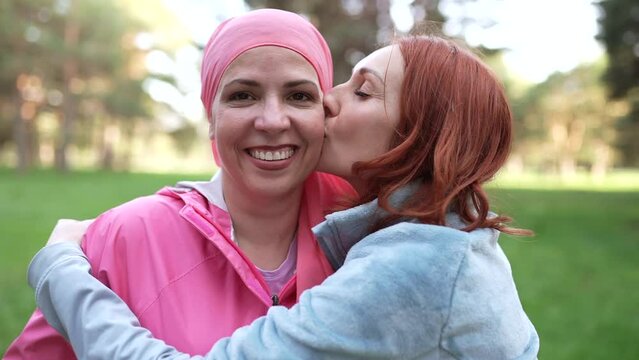 Cancer survivor woman with pink scarf hugging her friend, cancer treatment, fighting breast cancer