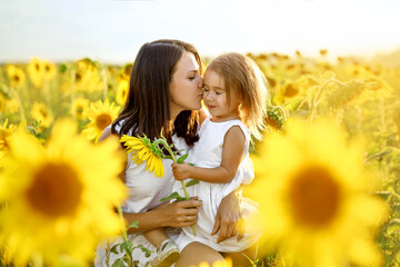 Mom gently kisses her little girl in gratitude for the gift of a sunflower flower for mother's Day....