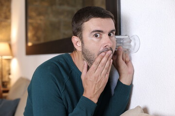 Man using glass to gossip through wall