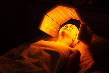 An elderly woman undergoes a facial rejuvenation procedure. Woman face lt Red light treatment At...