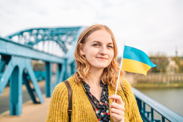 Happy young blonde girl in a beautiful dress holding a yellow-blue Ukrainian flag, standing on the...