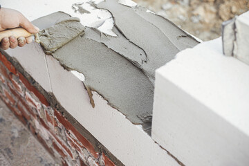 Builder installing masonry white blocks close up. Worker laying autoclaved aerated concrete blocks,...
