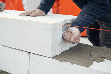 Masonry. Worker laying autoclaved aerated concrete blocks. Builder installing white blocks close...