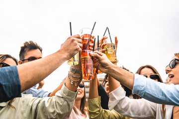Group of young friends raises plastic glasses with spritz and fruit cocktails for a celebrate toast...