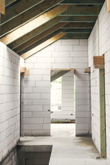 Unfinished attic wooden roof framing with vapor barrier, dormer and windows. View on timber rafters...