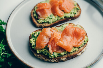 Toasted bread with mashed avocado and smoked salmon on grey plate