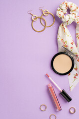 Obraz na płótnie Canvas Make up concept. Top view vertical photo of stylish scarf scrunchy lip gloss compact powder gold rings and earrings on isolated lilac background